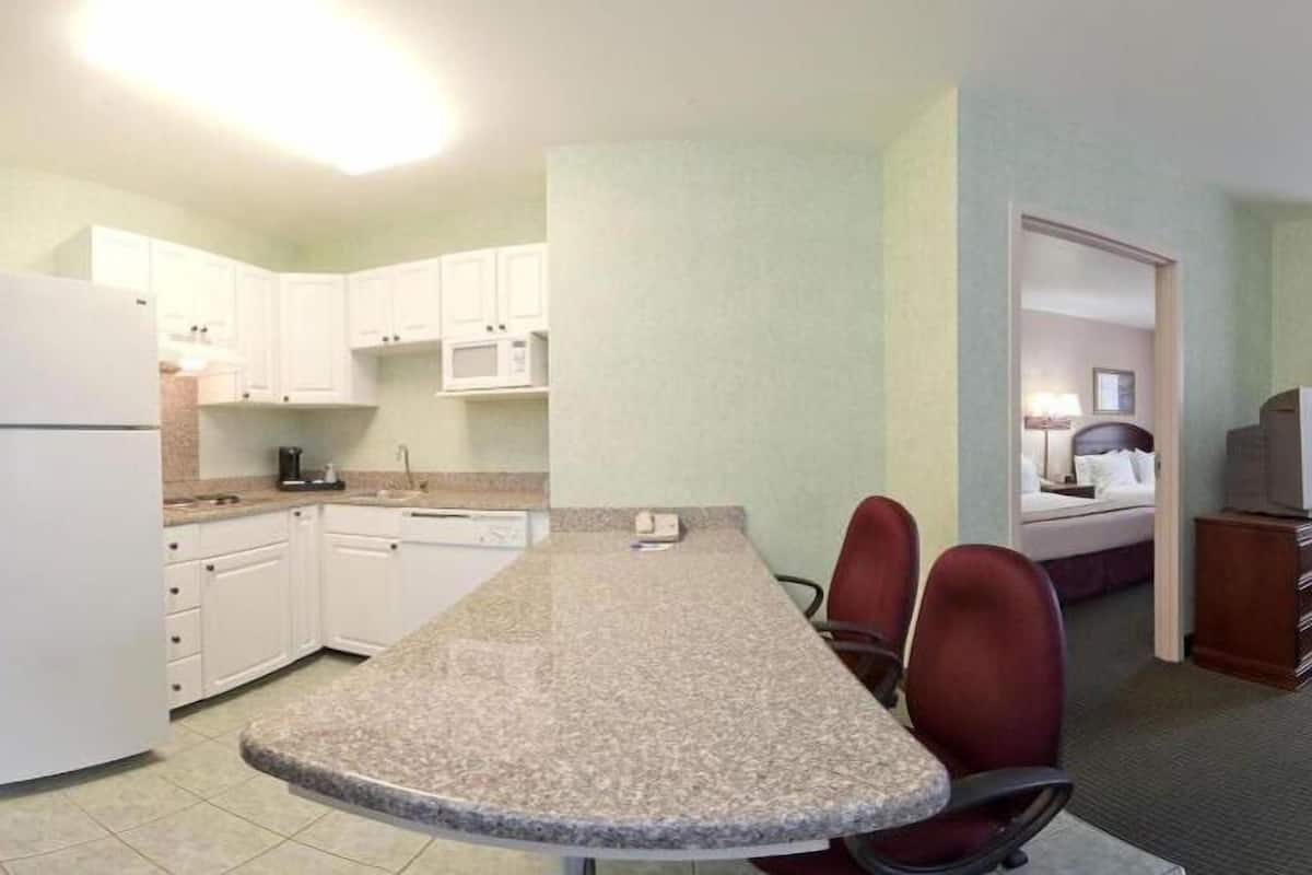 A compact kitchen with white cabinets, a microwave, and a refrigerator. There is a granite countertop with two chairs.