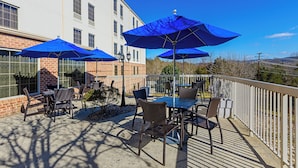 An outdoor patio with tables and chairs, blue umbrellas, and a white building in the background.