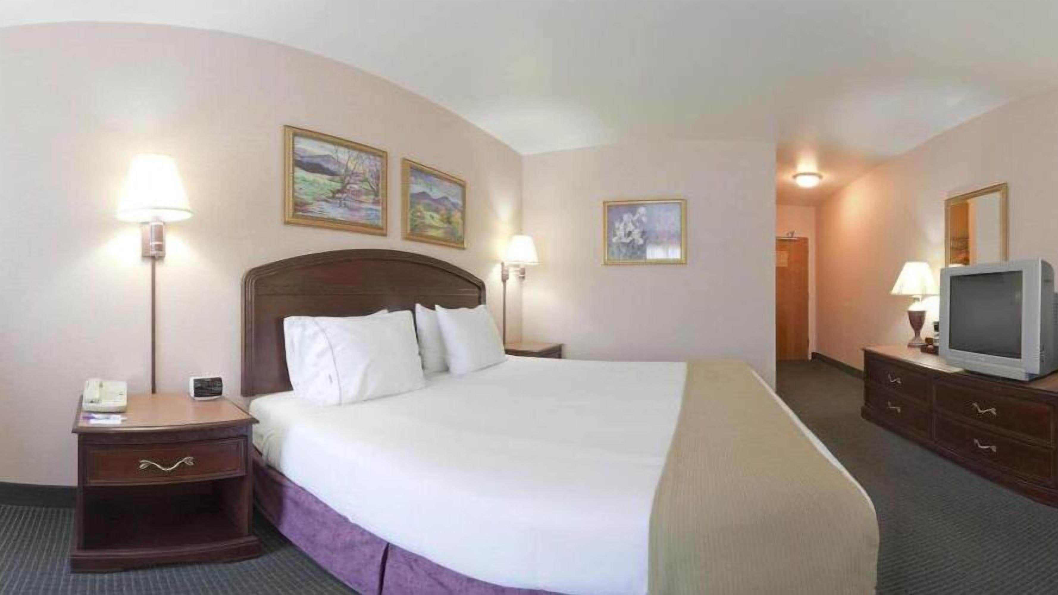 Quarto de hotel com uma cama grande, duas mesas de cabeceira, uma televisão e três quadros na parede.
