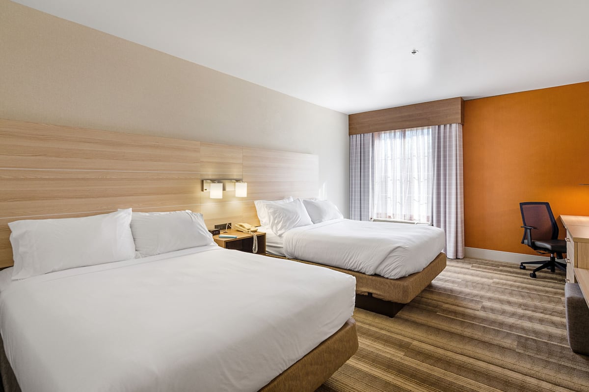 A hotel room with two beds, a desk, a chair, and a window with curtains.