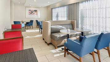 A hotel room with a sofa, two chairs, a small table, and a window with curtains.