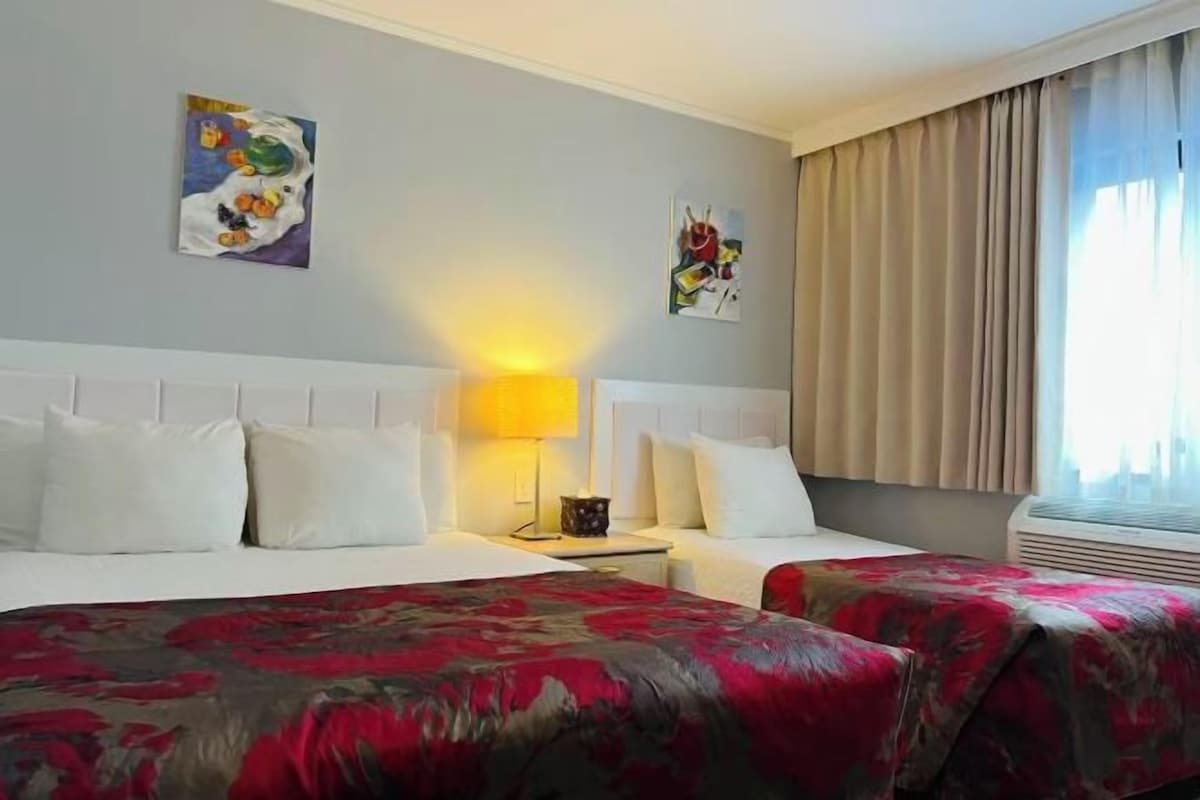 A hotel room with two beds, a nightstand, a lamp, and artwork on the walls.