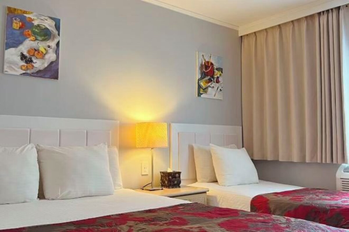 A hotel room with two beds, a nightstand, a lamp, and artwork on the walls.