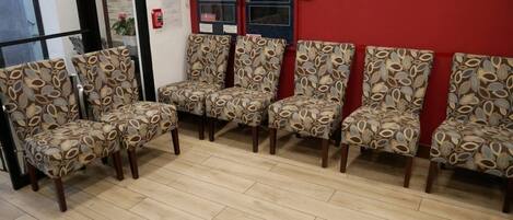A waiting area with six patterned chairs, a red wall, and a fire alarm.