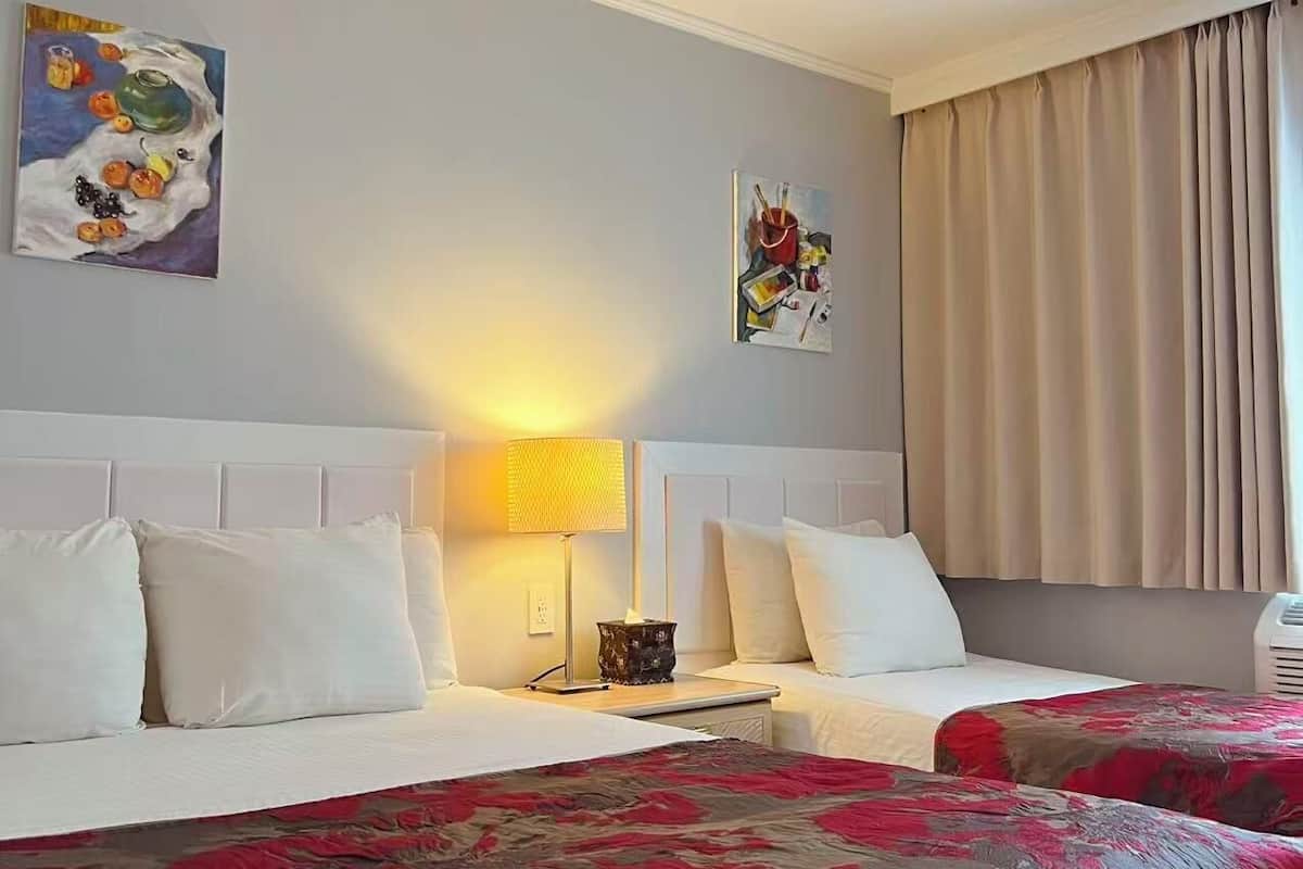 Habitación de hotel con dos camas, una mesita de noche, una lámpara y dos cuadros en la pared.