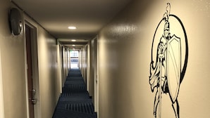 A hotel hallway with a patterned carpet, a wall-mounted security camera, and a wall decal of a knight. - Knights Inn Downtown Los Angeles (Los Angeles)