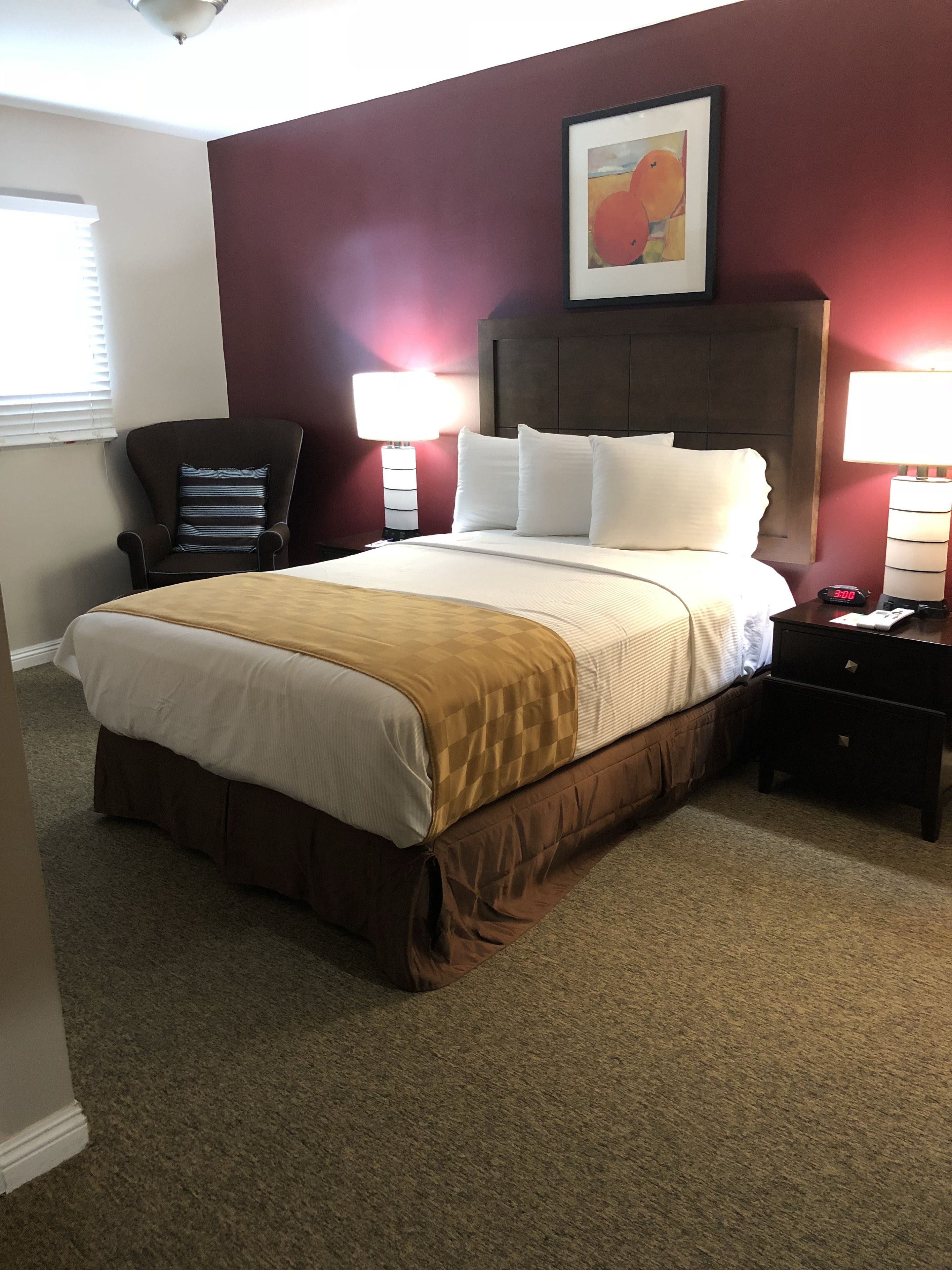A hotel room with a large bed, two bedside tables, a chair, and a painting on the wall.