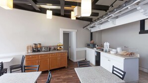 A modern kitchen with wooden cabinets, a central island, and a microwave. There are two tables with chairs, and the ceiling features exposed beams and pendant lights. - Knights Inn Downtown Los Angeles (Los Angeles)