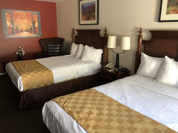 A hotel room with two beds, a nightstand with a lamp, a telephone, and a framed painting on the wall.