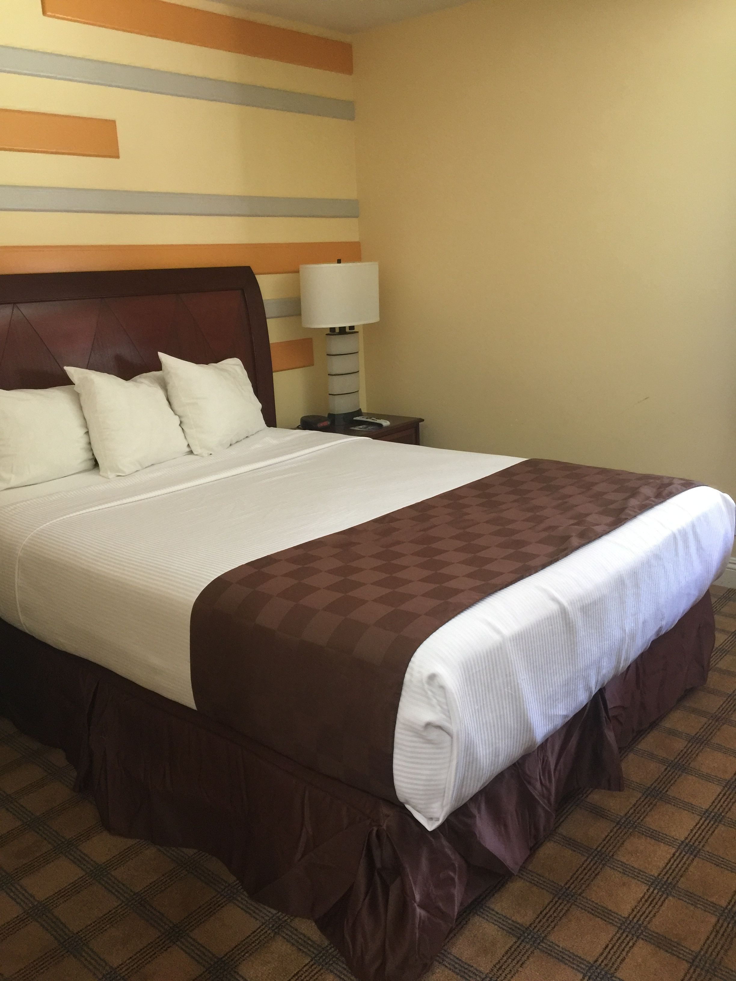 A hotel room with a large bed, a wooden headboard, a nightstand with a lamp, and a wall with horizontal stripes.