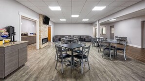 A spacious room with a kitchen area, multiple tables and chairs, and a stone accent wall.