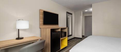 A hotel room with a bed, a desk with a lamp, a chair, a TV, and a wardrobe.