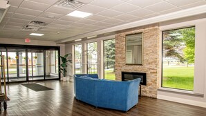 A lobby with a blue sofa, a fireplace, large windows, and a door with an exit sign.