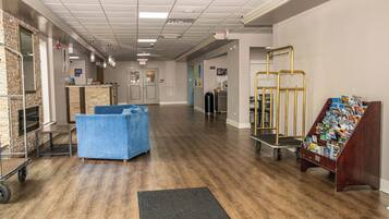 A spacious lobby with a blue sofa, a reception desk, a magazine rack, and a cart with a mat.