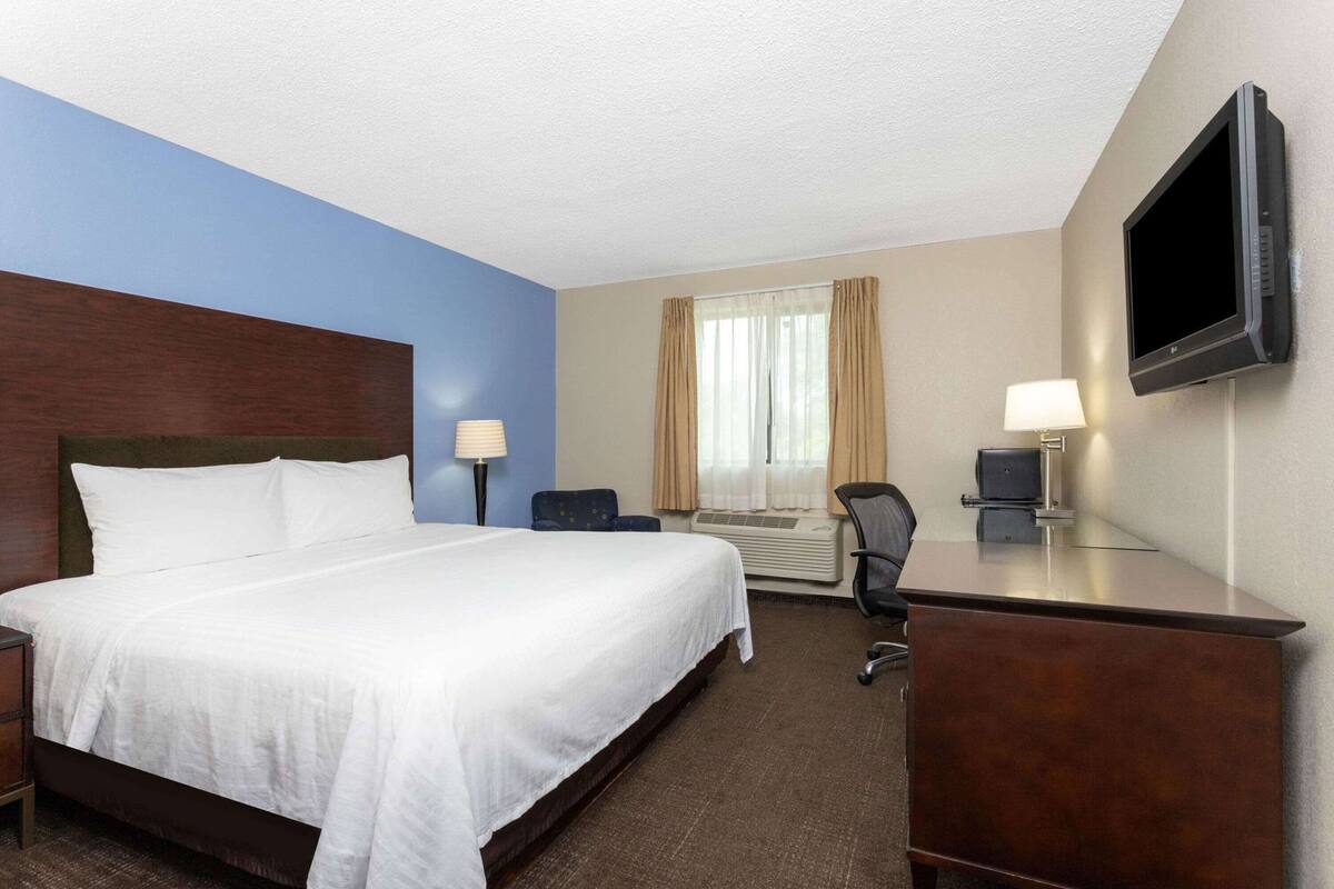A hotel room with a large bed, a desk, a chair, a flat-screen TV, and a window with curtains.