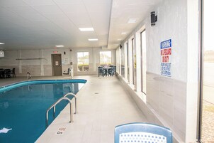 Una piscina interior con un cartel de advertencia para socorristas, sillas junto a la piscina y vistas al exterior.