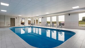 A large indoor swimming pool with clear blue water, surrounded by tiled flooring and equipped with multiple chairs and a sun lounger.