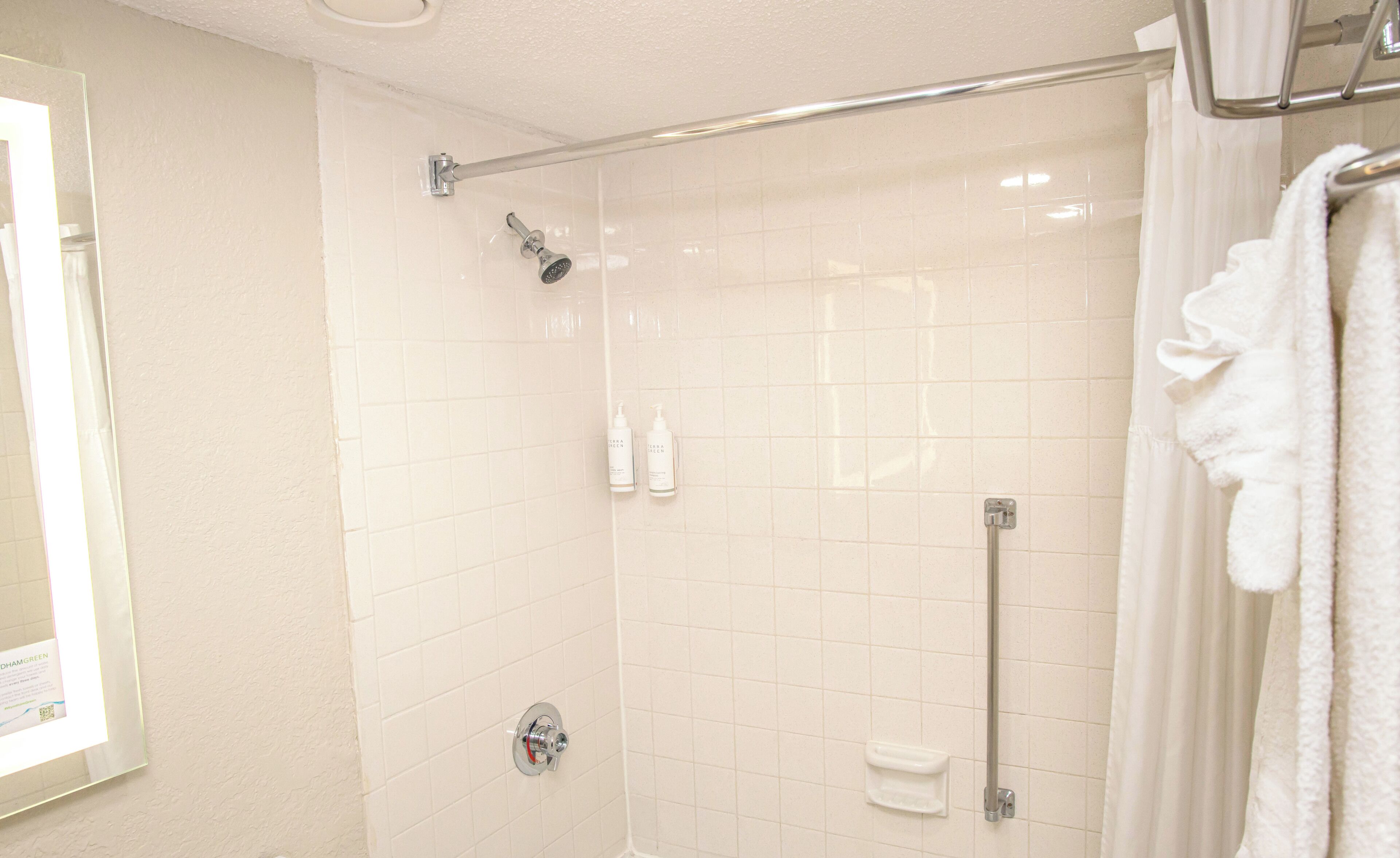 A shower with a glass door, a handrail, and a towel rack.