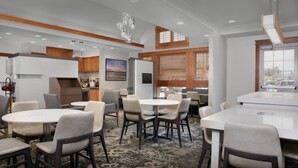 Un comedor de hotel moderno con mesas y sillas redondas, detalles de madera y amplias ventanas.