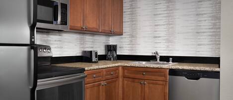 A kitchen with wooden cabinets, a stainless steel refrigerator, a microwave, an oven, a coffee maker, and a dishwasher.