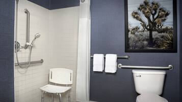 Un baño con ducha, inodoro, una silla y un cuadro enmarcado en la pared.