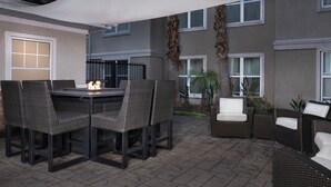 Un patio al aire libre con una mesa redonda y sillas, un dosel y vistas a un edificio con ventanas y una cerca.