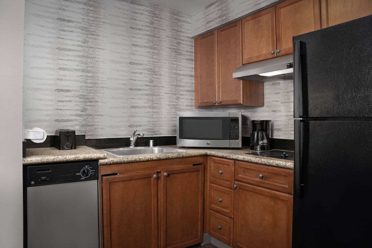 Una cocina con armarios de madera, un microondas de acero inoxidable, un refrigerador negro y un lavavajillas.