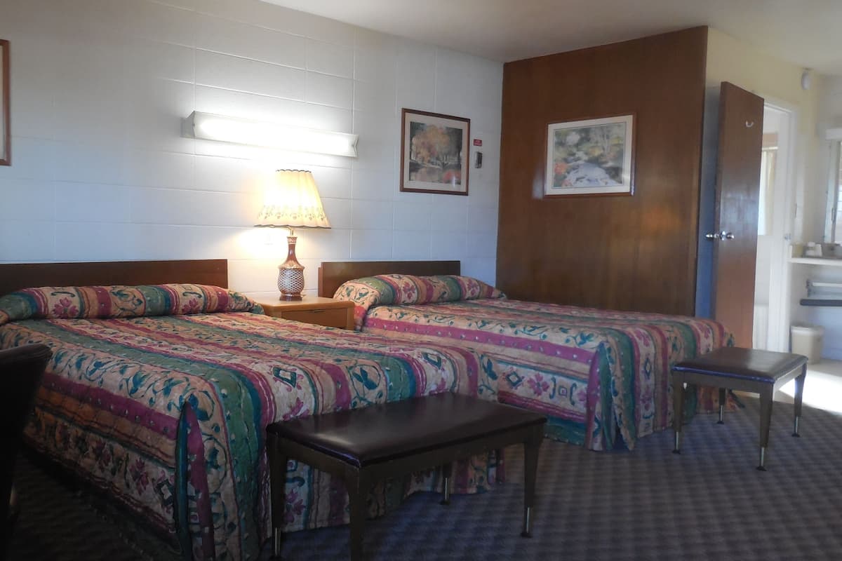 Habitación de hotel con dos camas, una mesita, una silla y una lámpara.