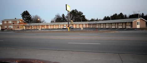 A motel with a row of rooms, a parking lot, and a building with a sign.
