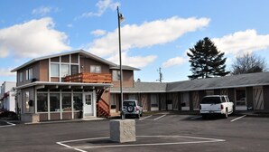 Un motel con estacionamiento, un área de estar al aire libre techada y un edificio con techo inclinado.