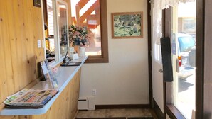 Zona de recepción con mostrador de madera, un jarrón de flores, un mapa enmarcado en la pared y vista de coches estacionados afuera.
