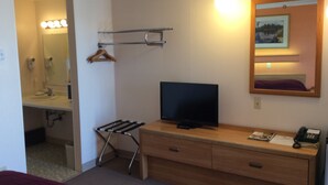 Una habitación de hotel con un escritorio de madera, televisión, teléfono y espejo con un cuadro.