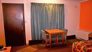 Una habitación pequeña con una mesa de madera y dos sillas, una cama con colcha estampada, una cortina azul y una pared naranja.
