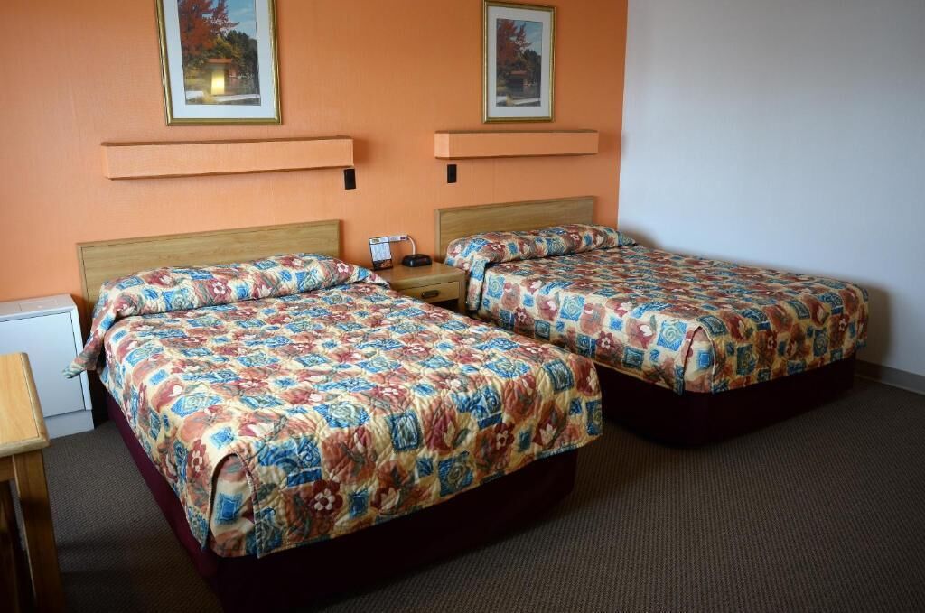 Een hotelkamer met twee bedden, elk voorzien van een bloemenprint beddegoed, een nachtkastje met een lamp en een klein tafeltje.