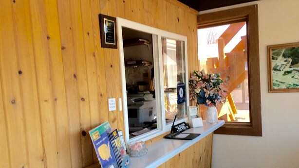 Un mostrador de recepción con un panel de madera en la pared, una ventana con vista a un edificio y un jarrón con flores.