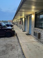 Fila de habitaciones de hotel con una pasarela techada y coches aparcados.