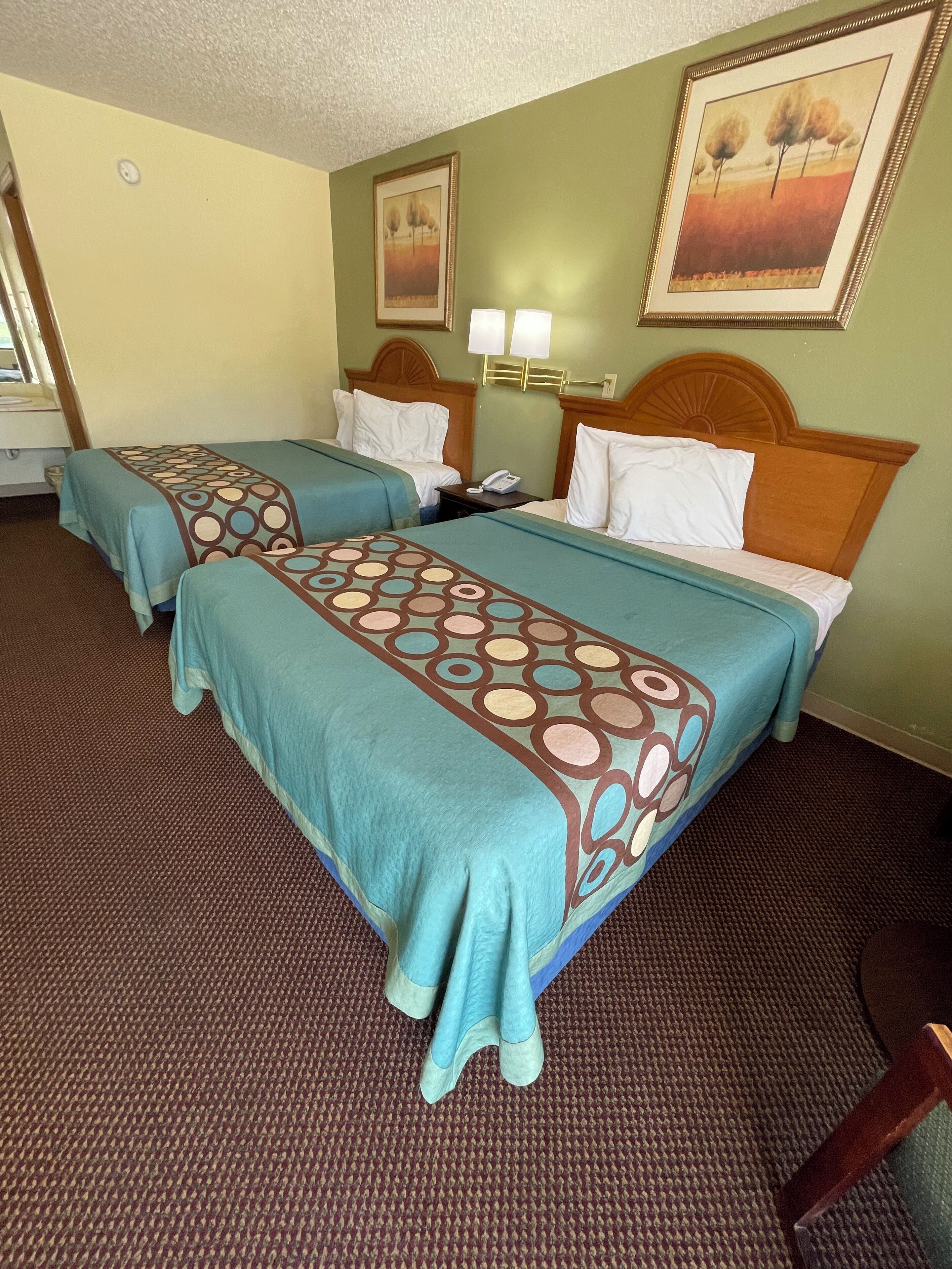 Habitación de hotel con dos camas, cada una con una colcha estampada, cabeceros de madera, una mesita de noche con lámpara y un cuadro en la pared.