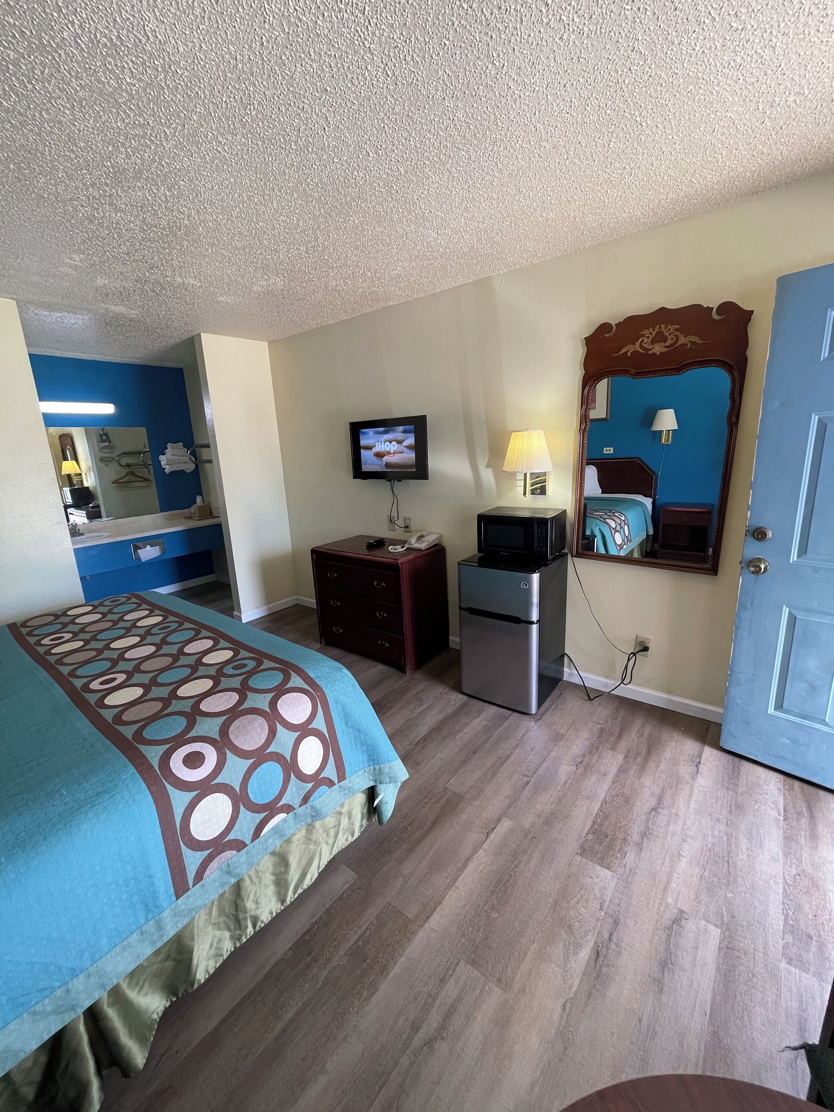 A hotel room with a bed, a desk, a television, a mirror, and a door.