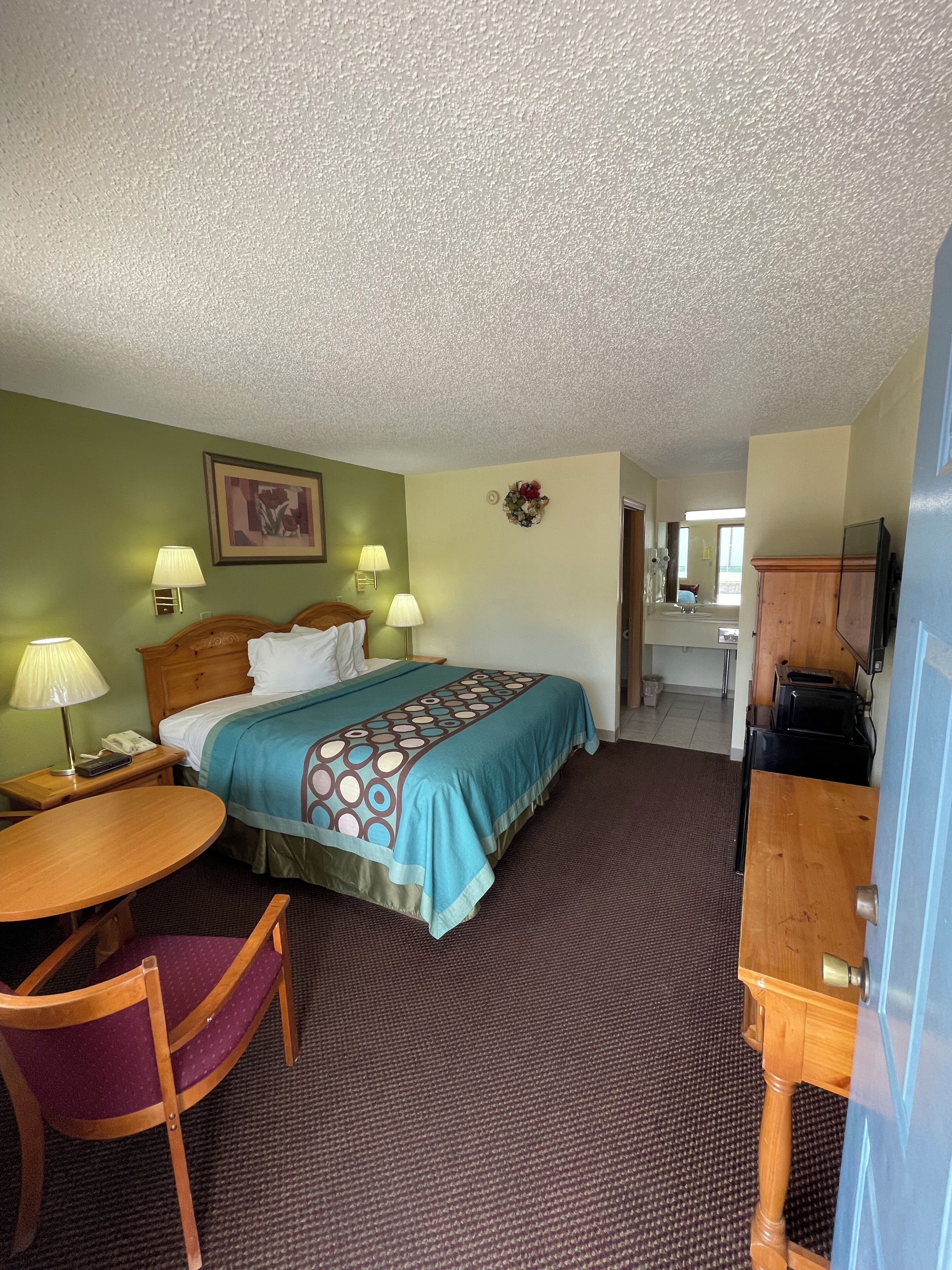 Quarto de hotel com uma cama, duas luminárias de cabeceira, uma mesa com cadeira e uma televisão.