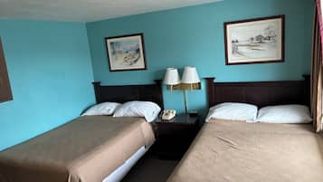 Een hotelkamer met twee bedden, een nachtkastje met een lamp, en twee ingelijste foto’s aan de wand.