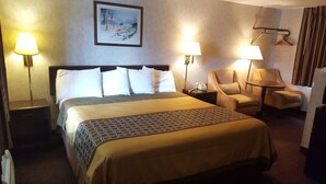 Une chambre d’hôtel avec un grand lit, deux lampes de chevet, une chaise, une petite table et un tableau au mur.