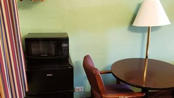 A compact room with a kitchenette, a dining table with a lamp, and a chair.