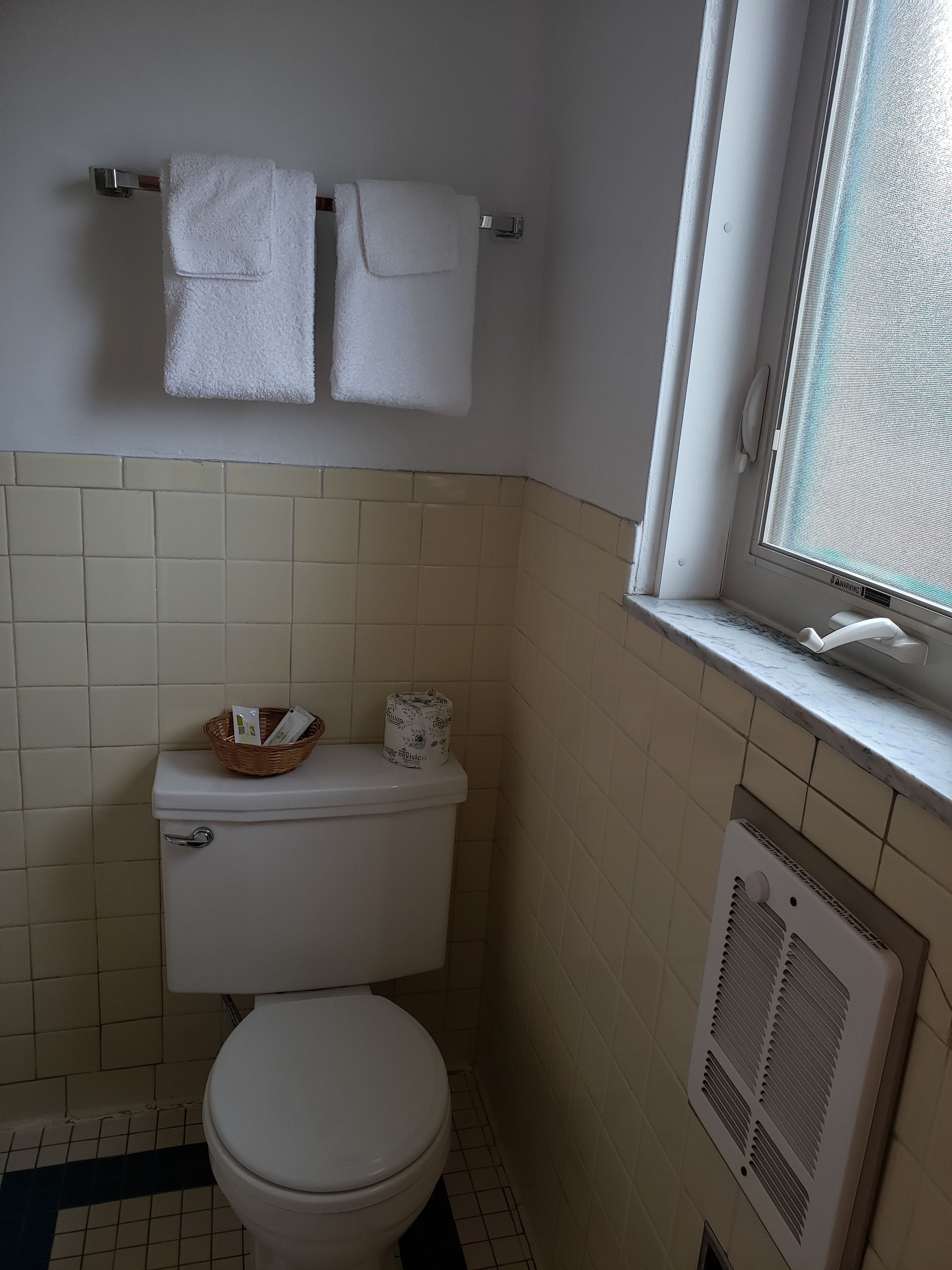 Un baño pequeño con inodoro, ventana y un perchero con dos toallas.