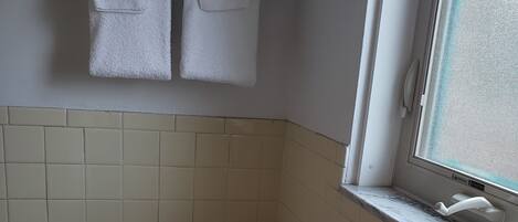 Une petite salle de bain comprenant des toilettes, une fenêtre et un porte-serviettes avec deux serviettes.