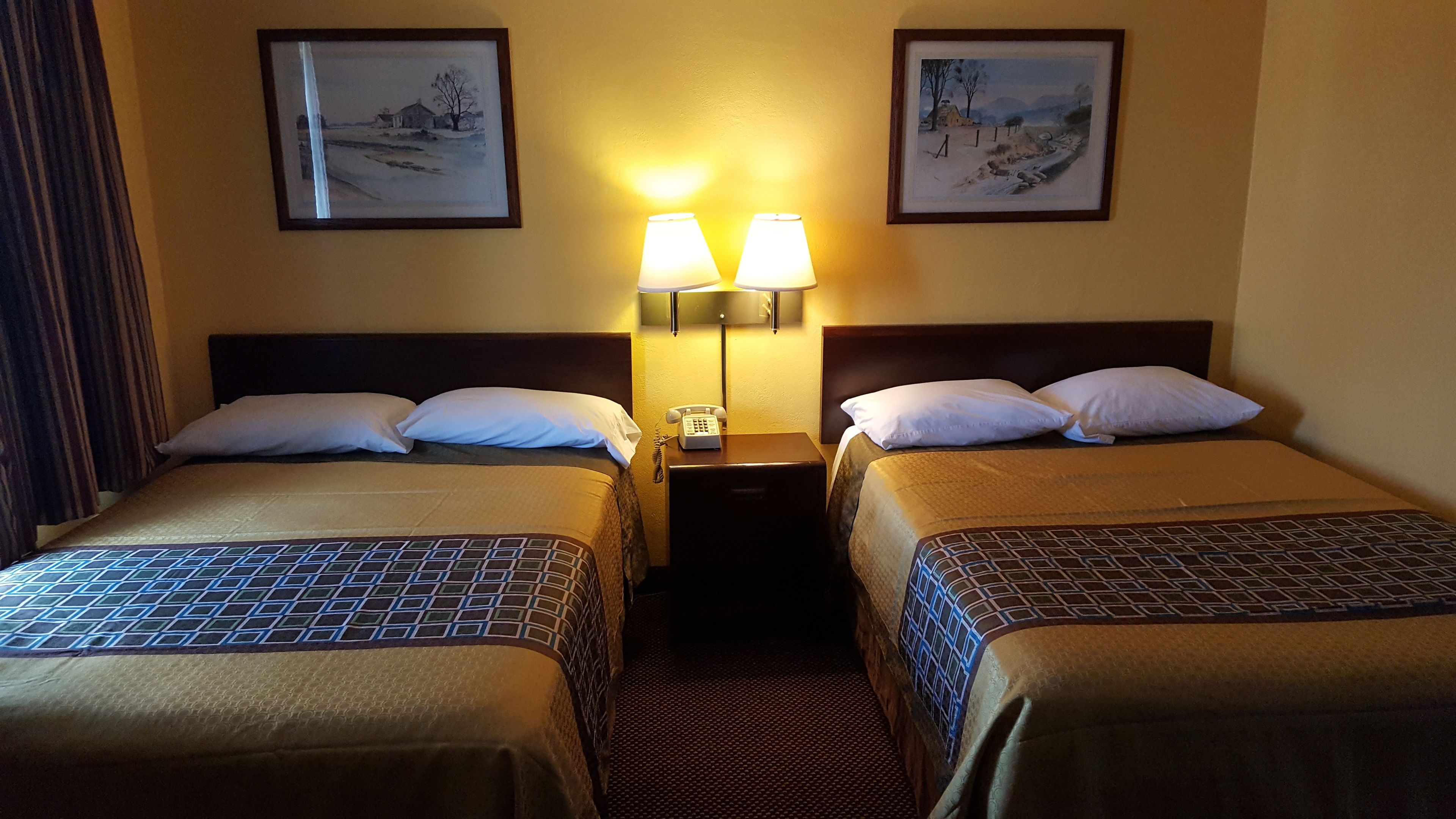 A hotel room with two beds, a nightstand with a lamp, and two framed pictures on the wall.