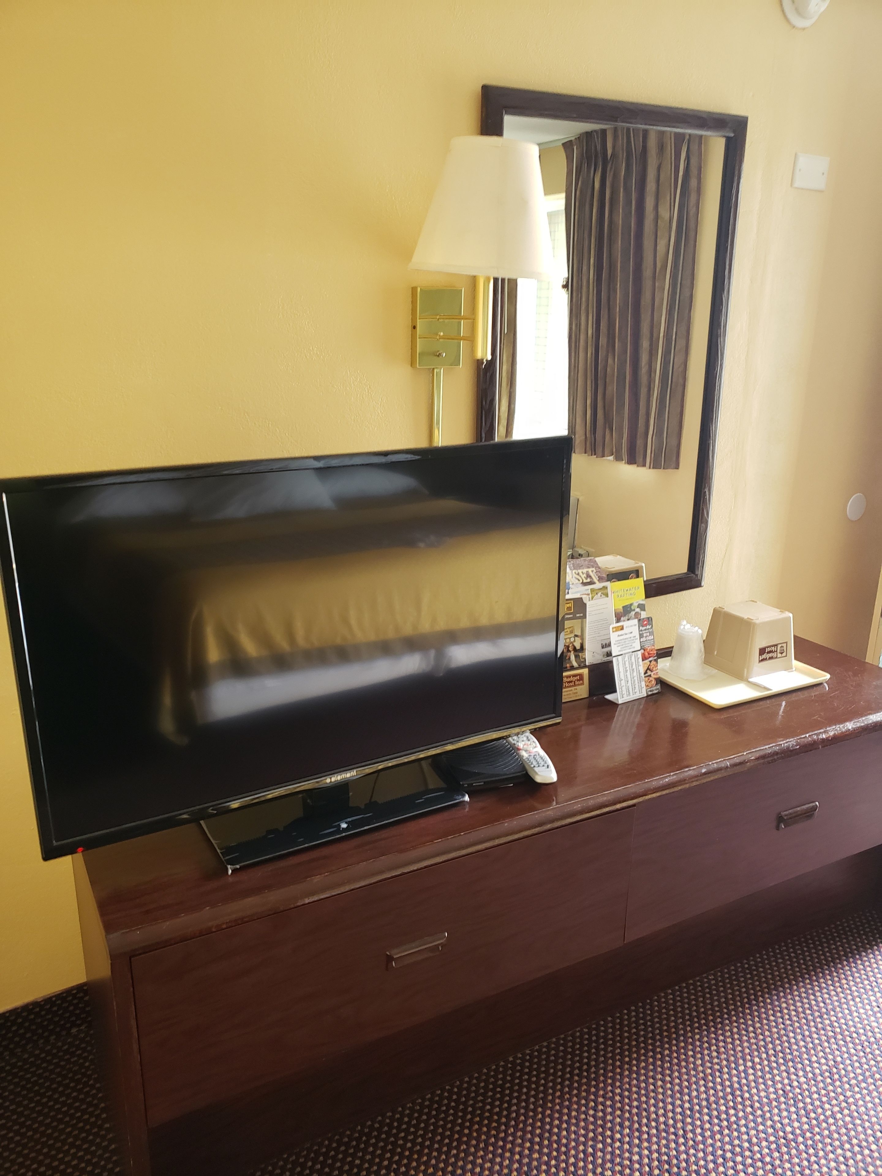 Un televisor sobre un tocador de madera, una lámpara, un espejo y algunos artículos de aseo.