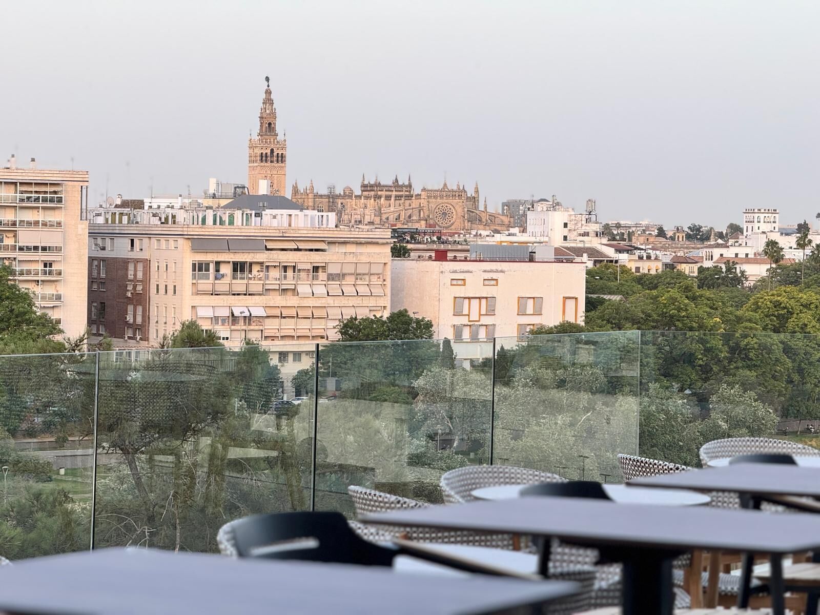 Eine Terrasse mit Tischen und Stühlen, die auf einen Stadtblick mit historischen Gebäuden und einem markanten Turm ausgerichtet ist.