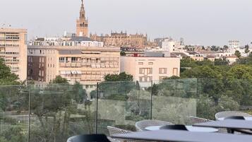 Eine Terrasse mit Tischen und Stühlen, die auf einen Stadtblick mit historischen Gebäuden und einem markanten Turm ausgerichtet ist.