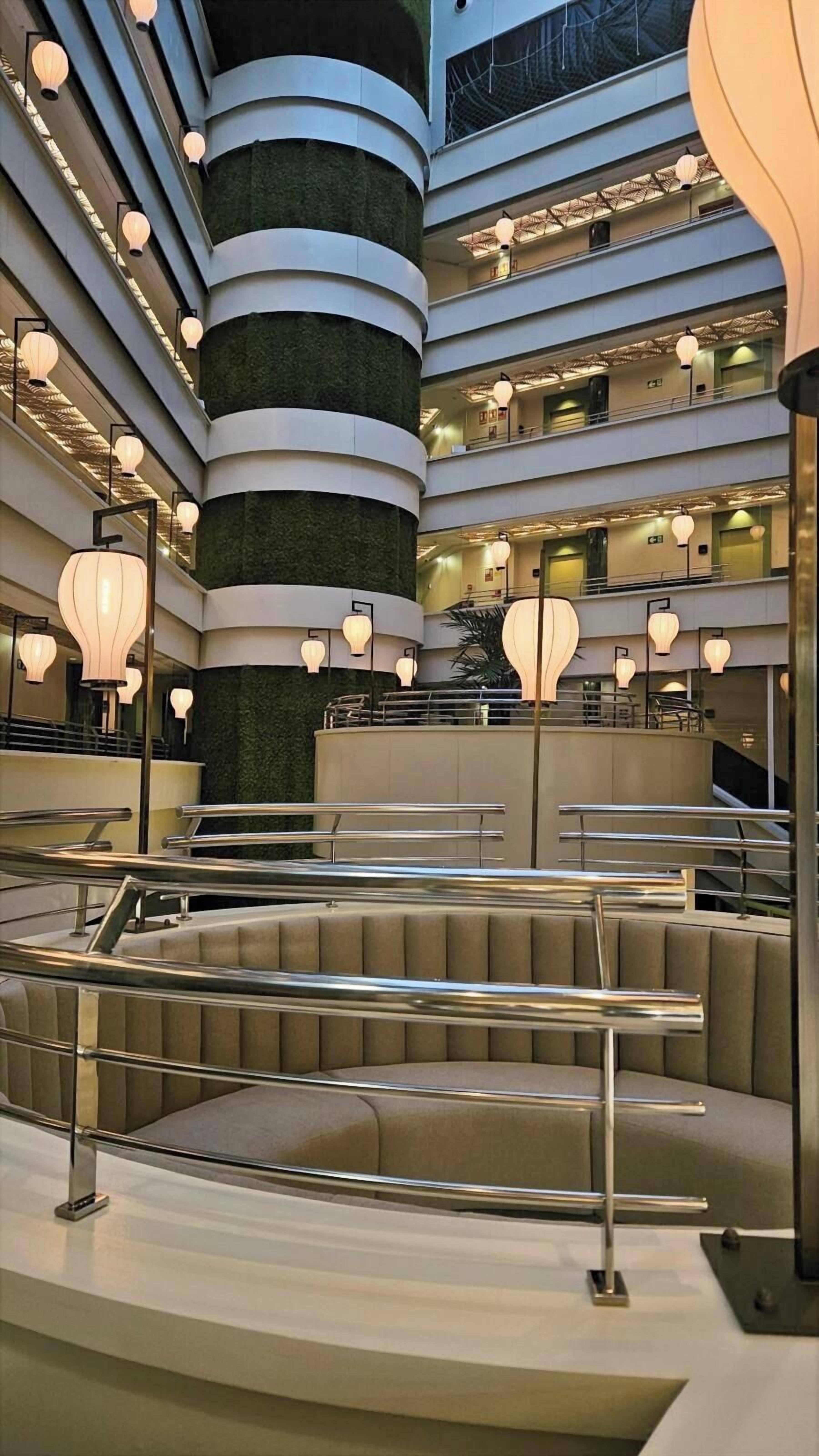 Un atrio de varios niveles con arquitectura moderna, que presenta una escalera espiral central, zonas de asientos escalonados e iluminación ambiental.