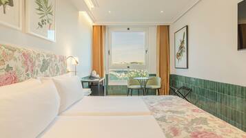A hotel room with a large bed, a desk with a chair, a small table, and a window with a view.
